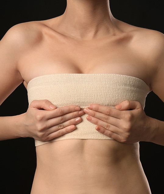 Woman wrapping bandages around chest after breast lift and reduction