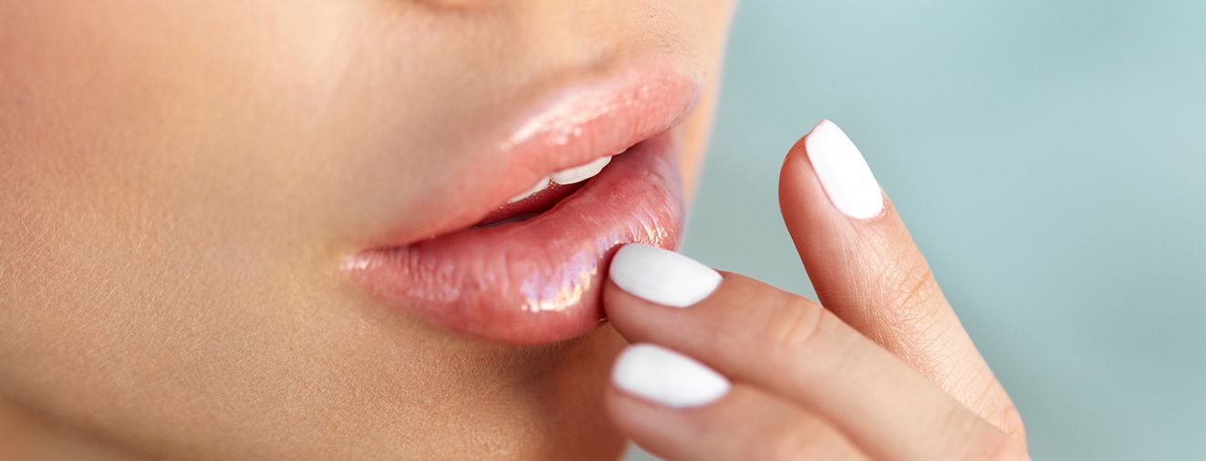 Person touching a fingertip to plump lips after filler treatment