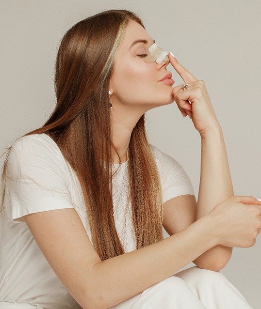Woman touching her bandaged nose after rhinoplasty